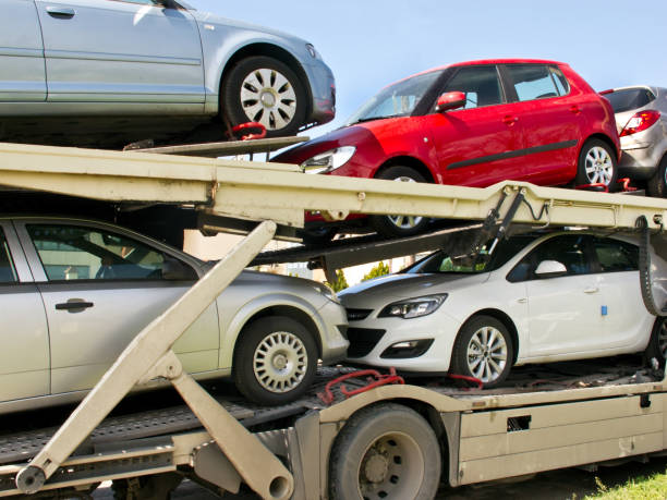 A car transporter truck carrying several cars on two levels—including red, white, silver, and gray vehicles—travels under a clear blue sky. This scene perfectly captures the reliable service of NY Auto Transport Fulton, NY professionals who specialize in secure and efficient vehicle shipping.